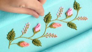 Completed floral hand embroidery on pastel fabric with satin leaves and rosebuds