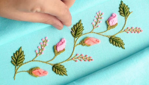 Completed floral hand embroidery on pastel fabric with satin leaves and rosebuds